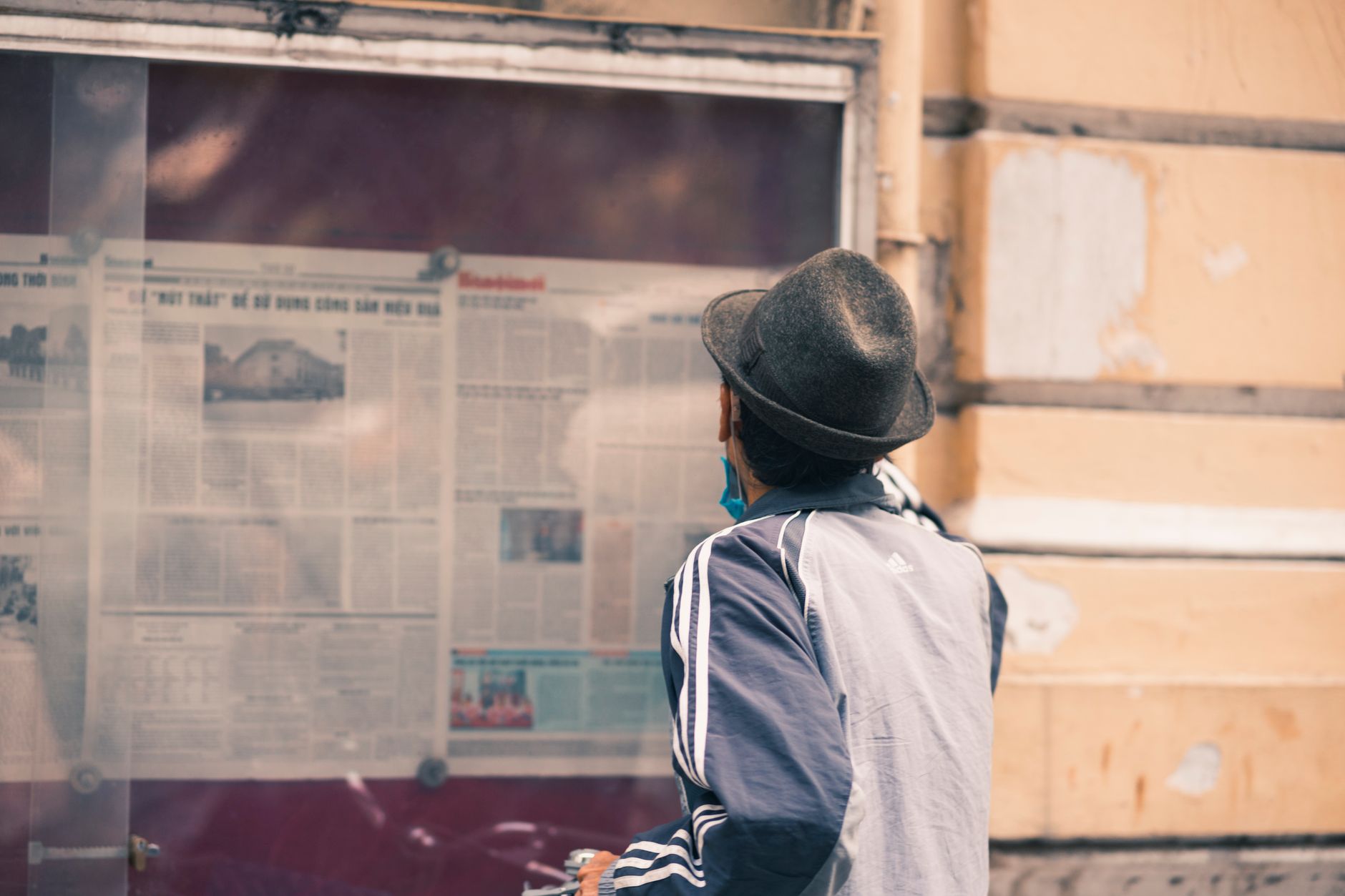 A man in a hat reads a newspaper on an outdoor message board. — 7 Benefits of Breast Augmentation