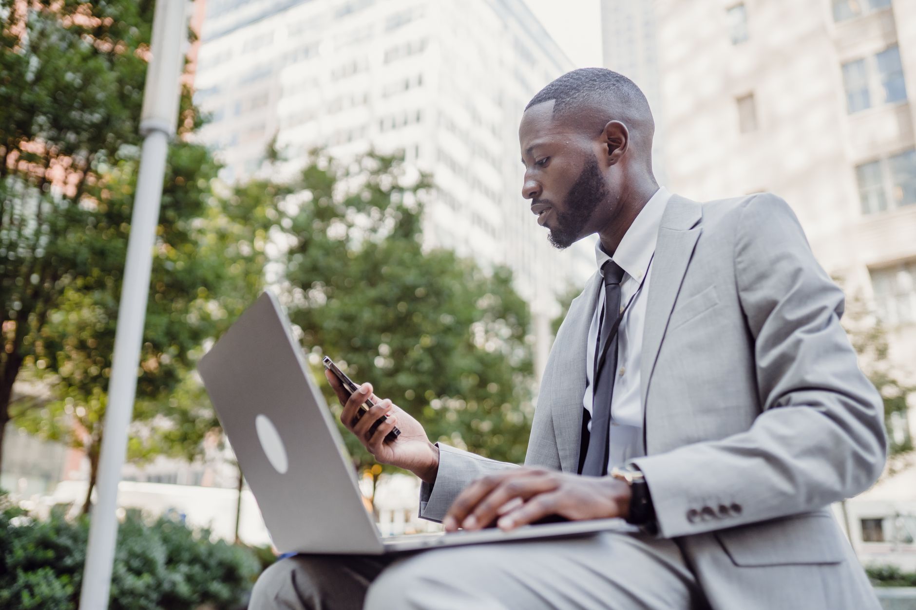 Businessman in a suit using a laptop and smartphone in an urban setting, blending technology with business. — Analyzing the S