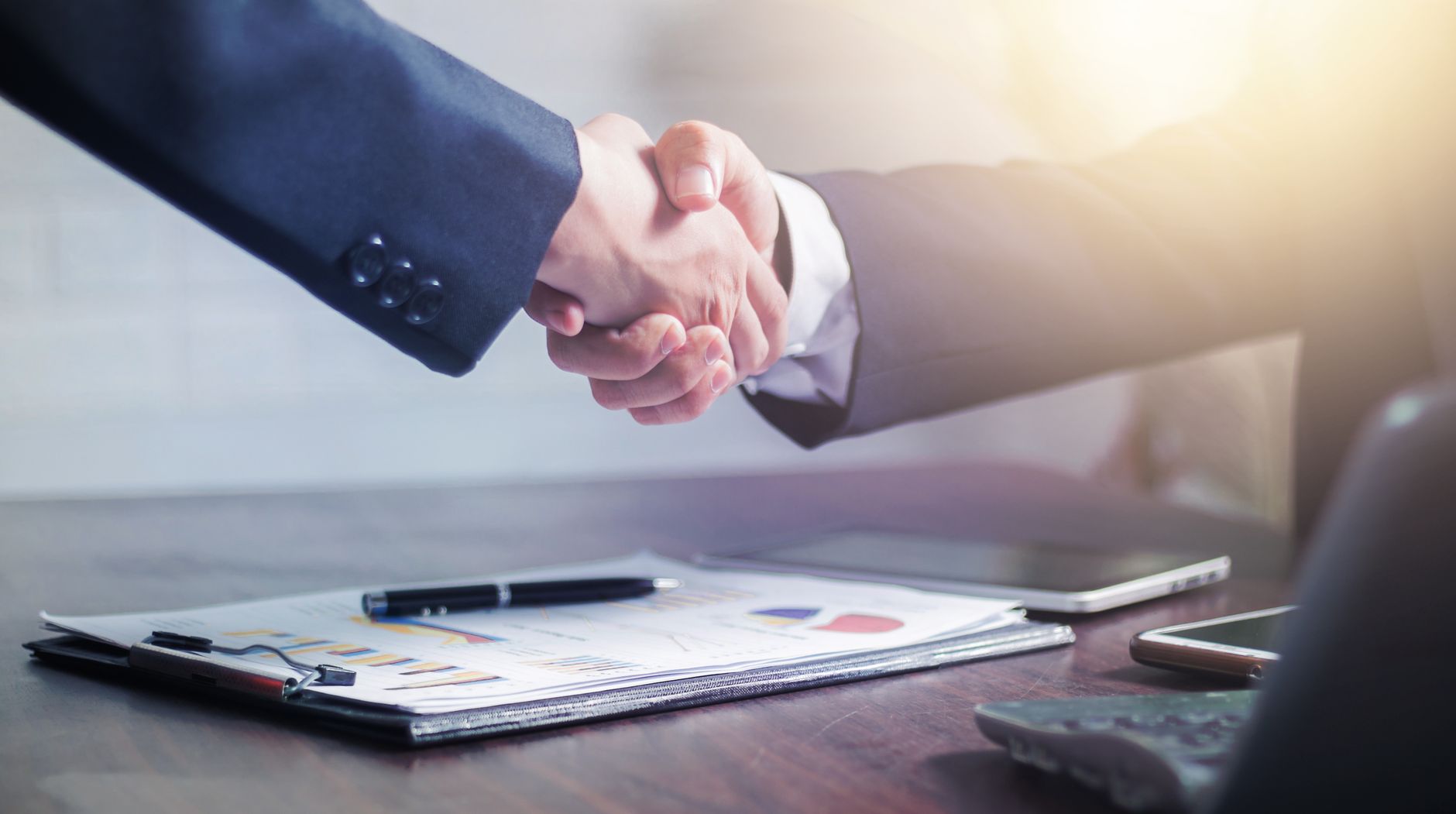 Professional handshake agreement over business charts in an office setting. — Domain Auctions: How to Win Your Preferred Web