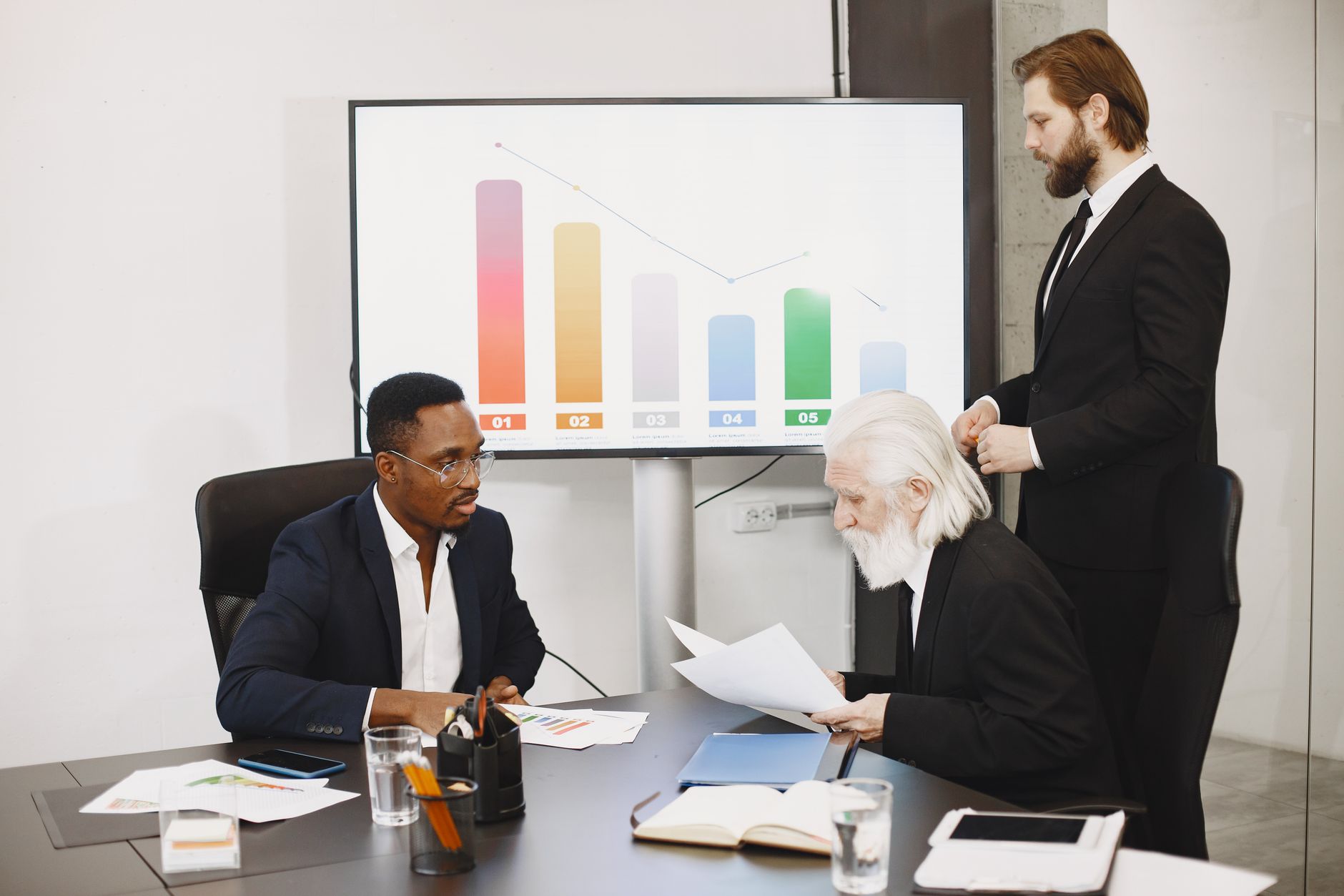 Three businessmen discussing financial data in a modern office setting with charts. — Drug Rehab in Phoenix: A Guide to the P