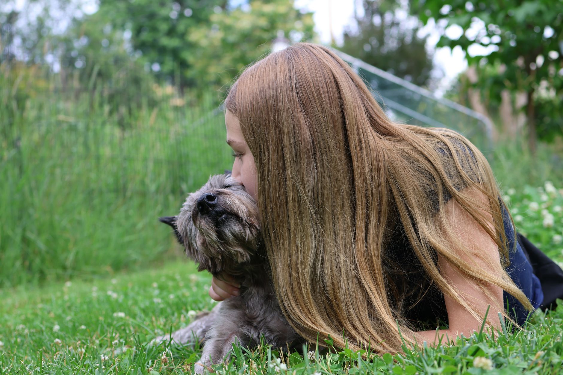 A young girl affectionately embraces her dog in a lush summer garden, conveying warmth and companionship. — Everything You Ne