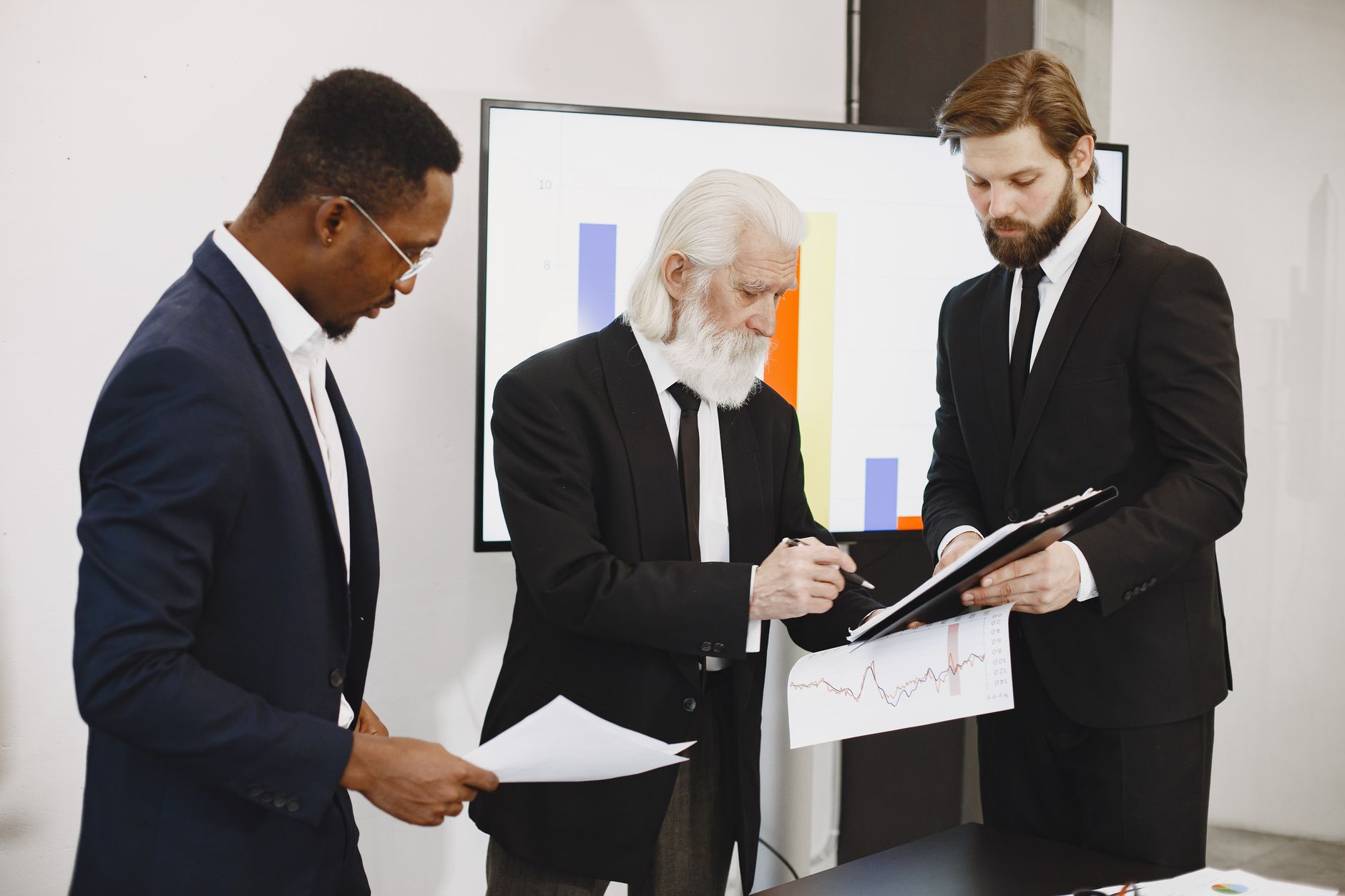 Three businessmen in suits reviewing reports and graphs during an office meeting. — Feel The Magic Of Xbox Name Generator