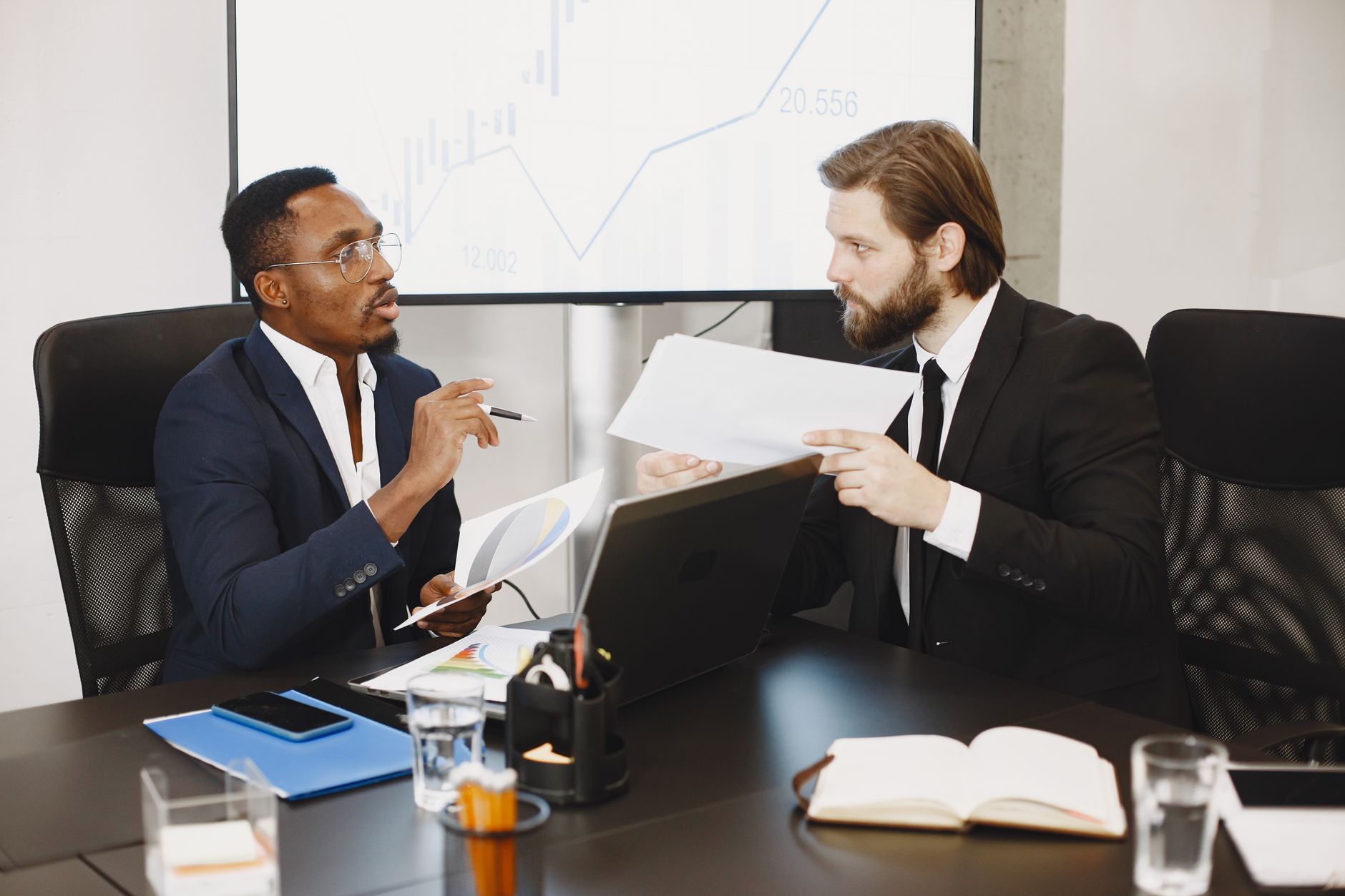 Two business professionals engaged in a planning meeting, discussing documents in a modern office setting. — Get to know in d
