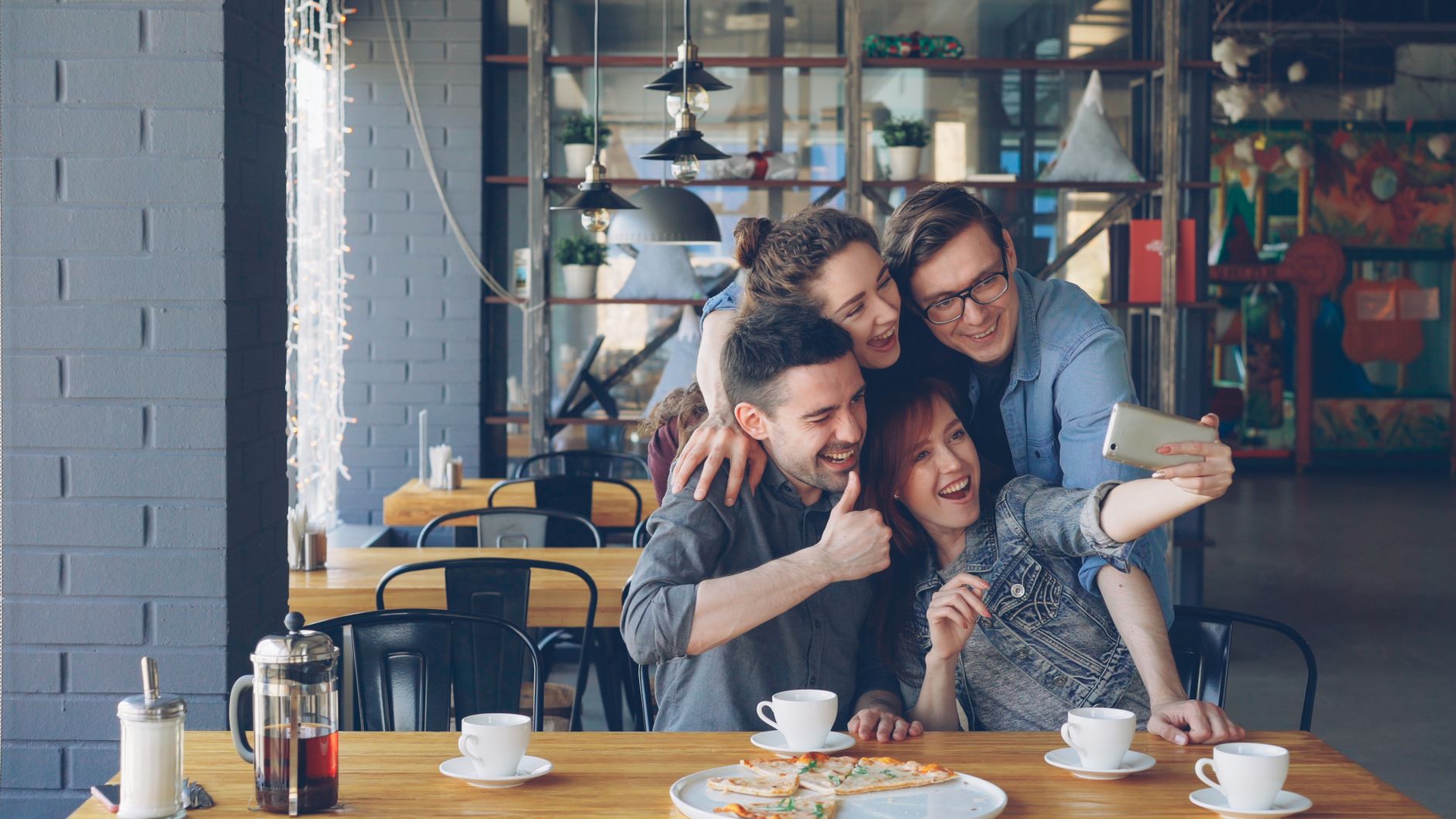Group of friends taking a selfie at a café while enjoying coffee and pizza. — How Buying Instagram Followers Helps Business S