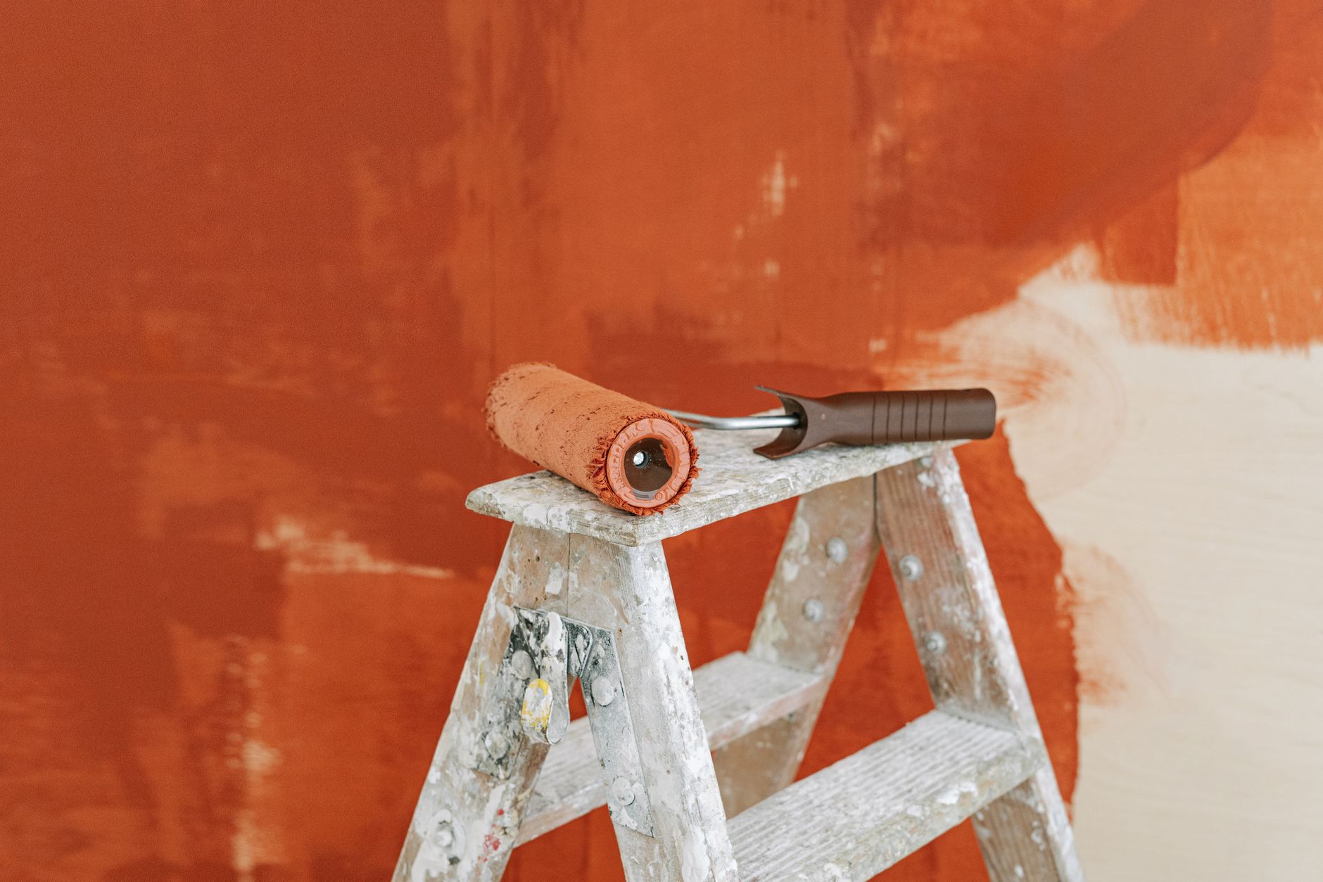 Paint roller on a ladder with a partially painted red wall in the background. — How to Layer Lighting in Your Home Office for