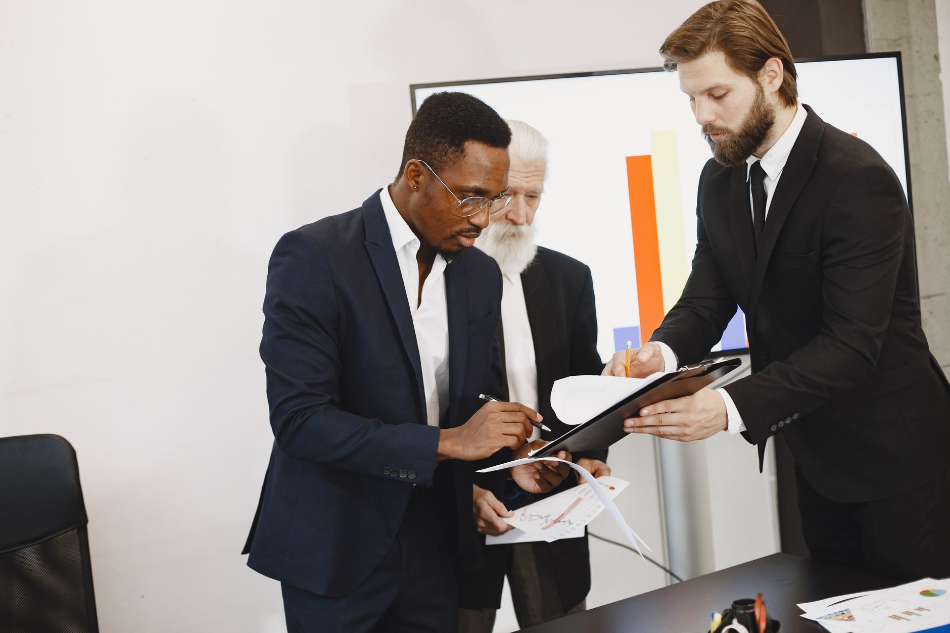 Three businessmen engaged in document signing in a modern office setting. — How To Take Advantage Of Better Maine VA Mortgage
