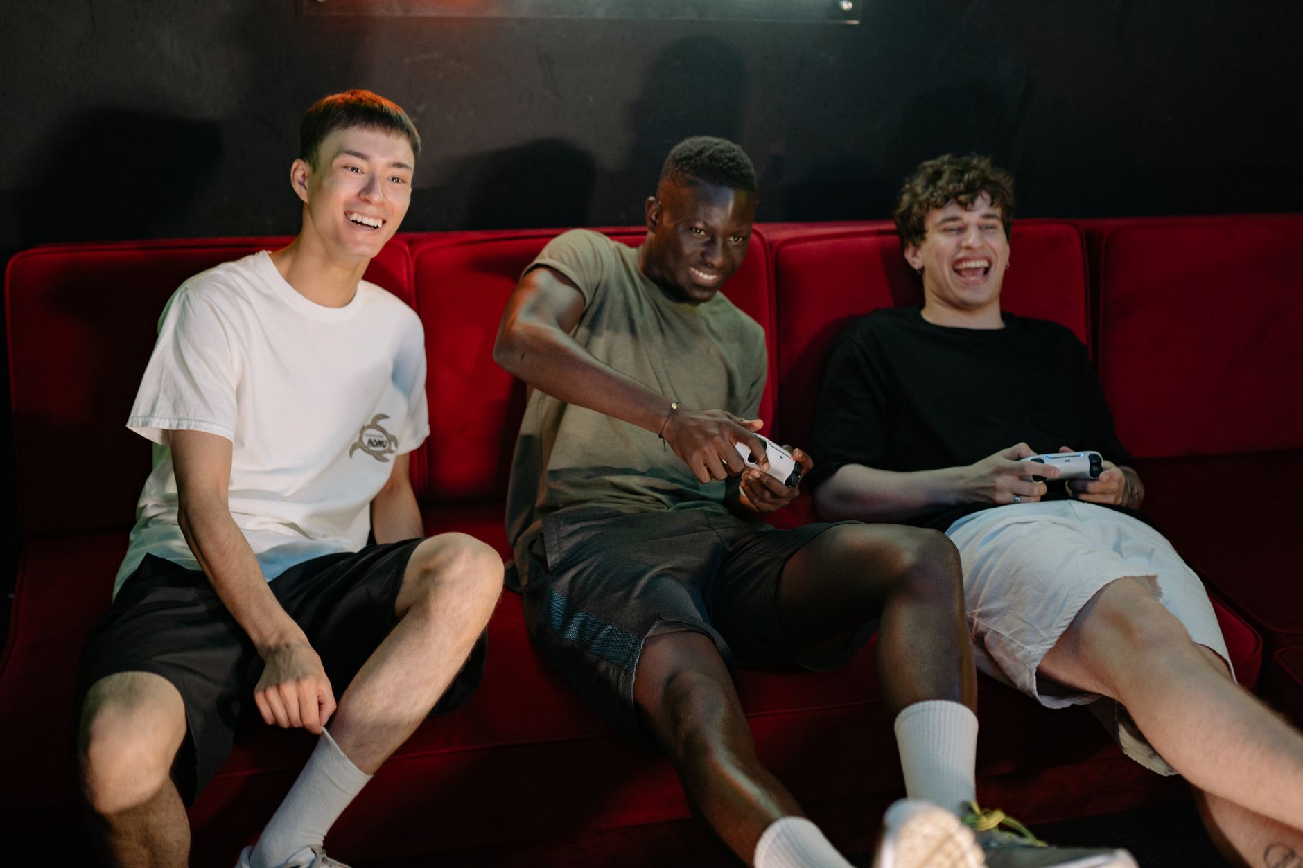 Three diverse young men sitting on a red couch, enjoying a fun video game session together. — How Verification Protects Onlin