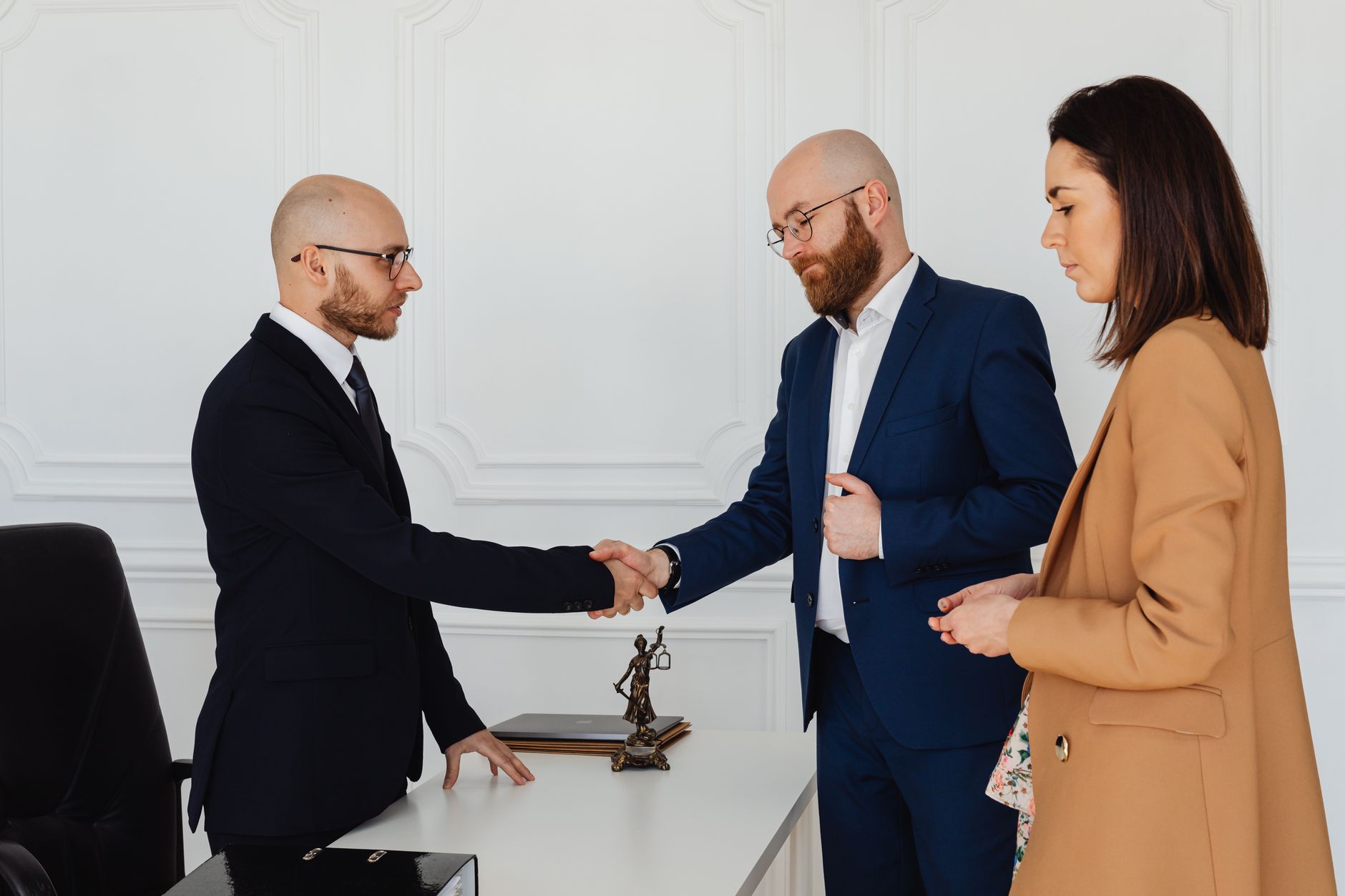 Three business professionals in formal attire shake hands during an office meeting. — Injured in an auto accident in Queens?