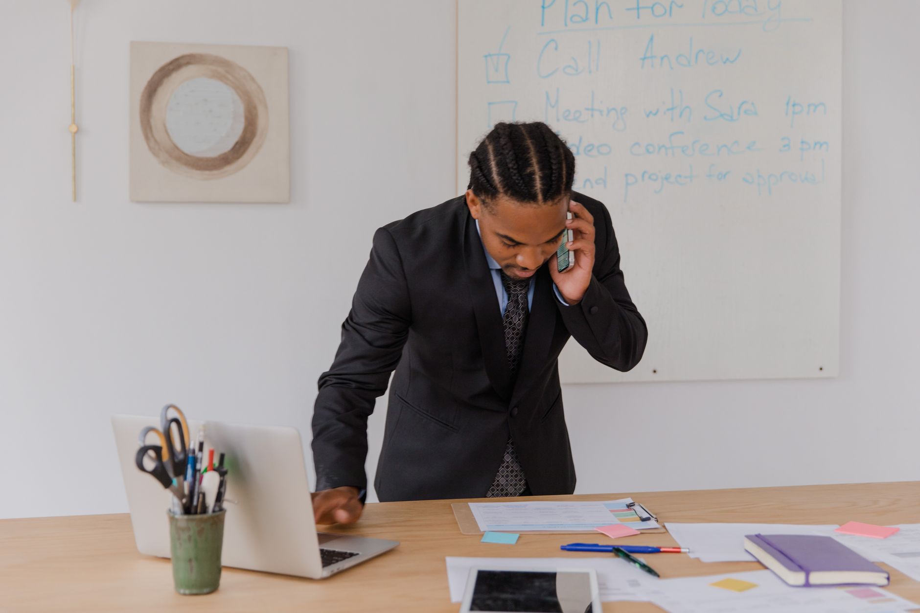 Professional businessman multitasking with phone and laptop at office desk, surrounded by documents. — Innovations in Motion: