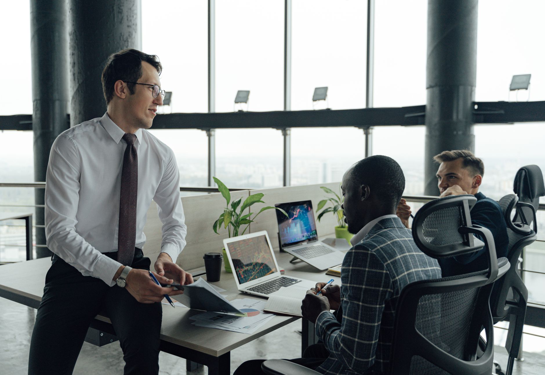 Three men engaged in a business meeting in a modern office setting with laptops and documents. — Luxury All-Purpose Damascus