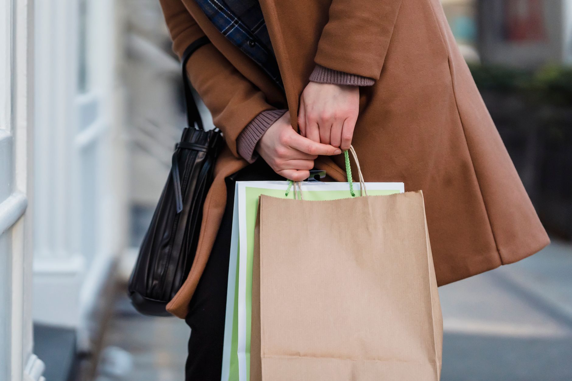 Crop unrecognizable female customer wearing coat standing with paper packets and handbag while shopping in city — Name a Star
