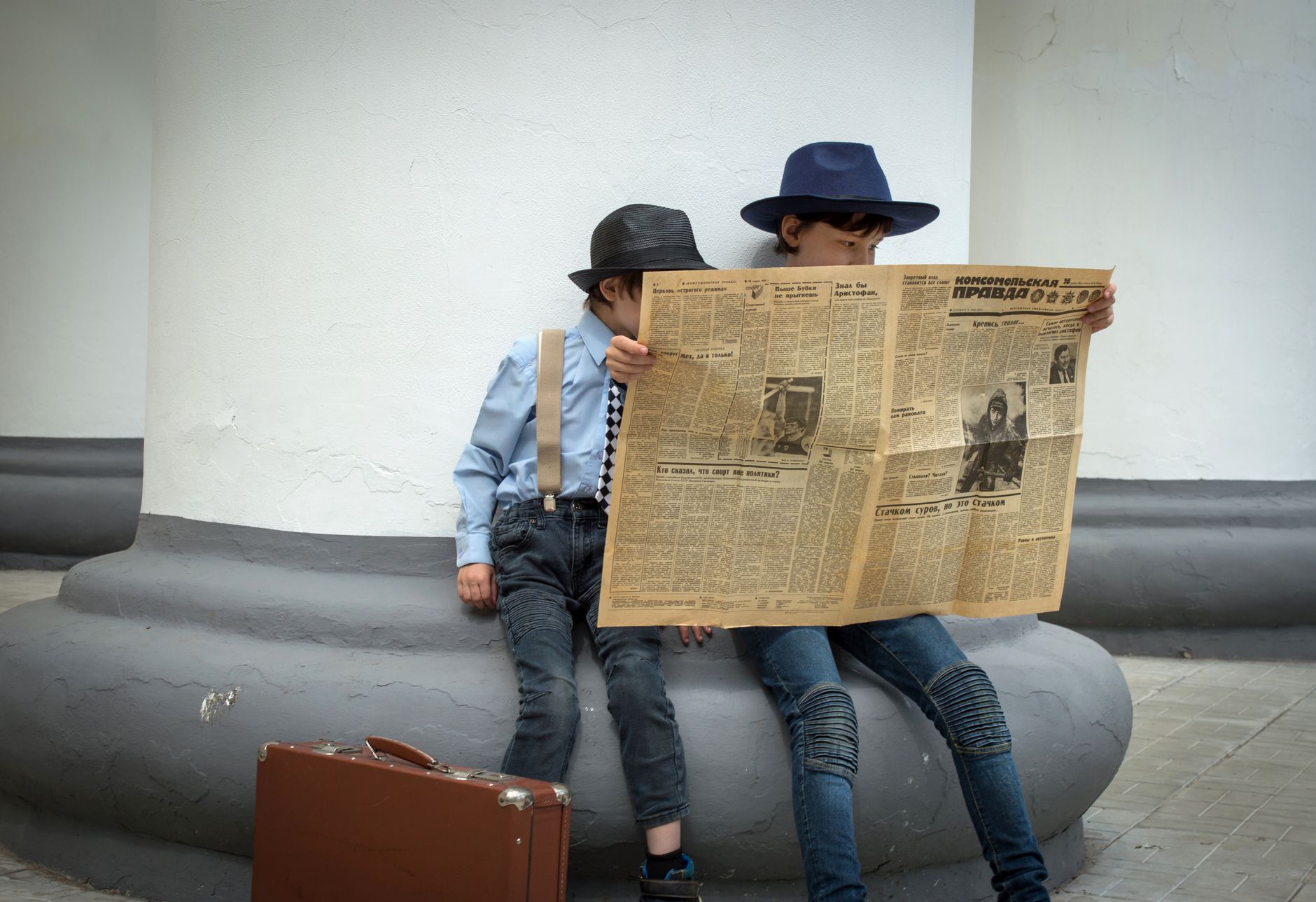 Two stylish children in hats reading a vintage newspaper outdoors. — Navigating Immigration Laws with Edmonton's Best Consult