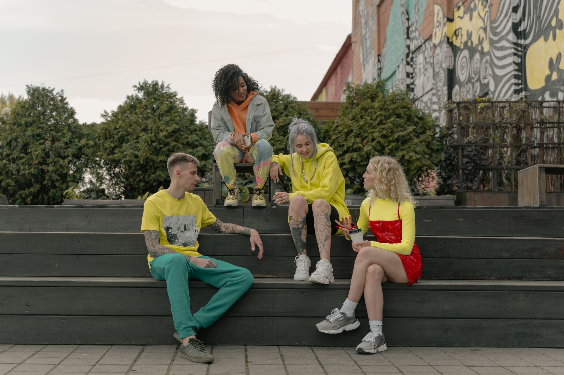 Group of young adults relaxing and chatting on steps in front of colorful street art. — Pants Men Must Have