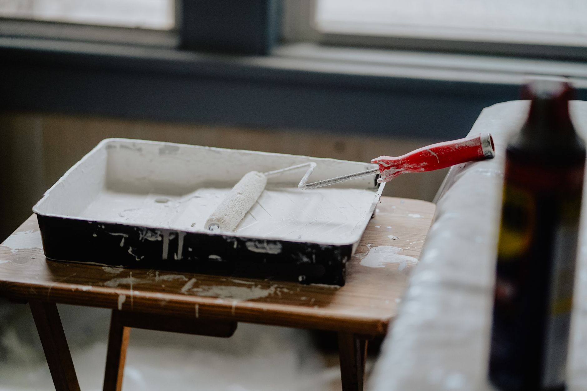 A paint roller and tray with white paint on a wooden table, indicating a renovation work. — Pros Of Sisal Rugs