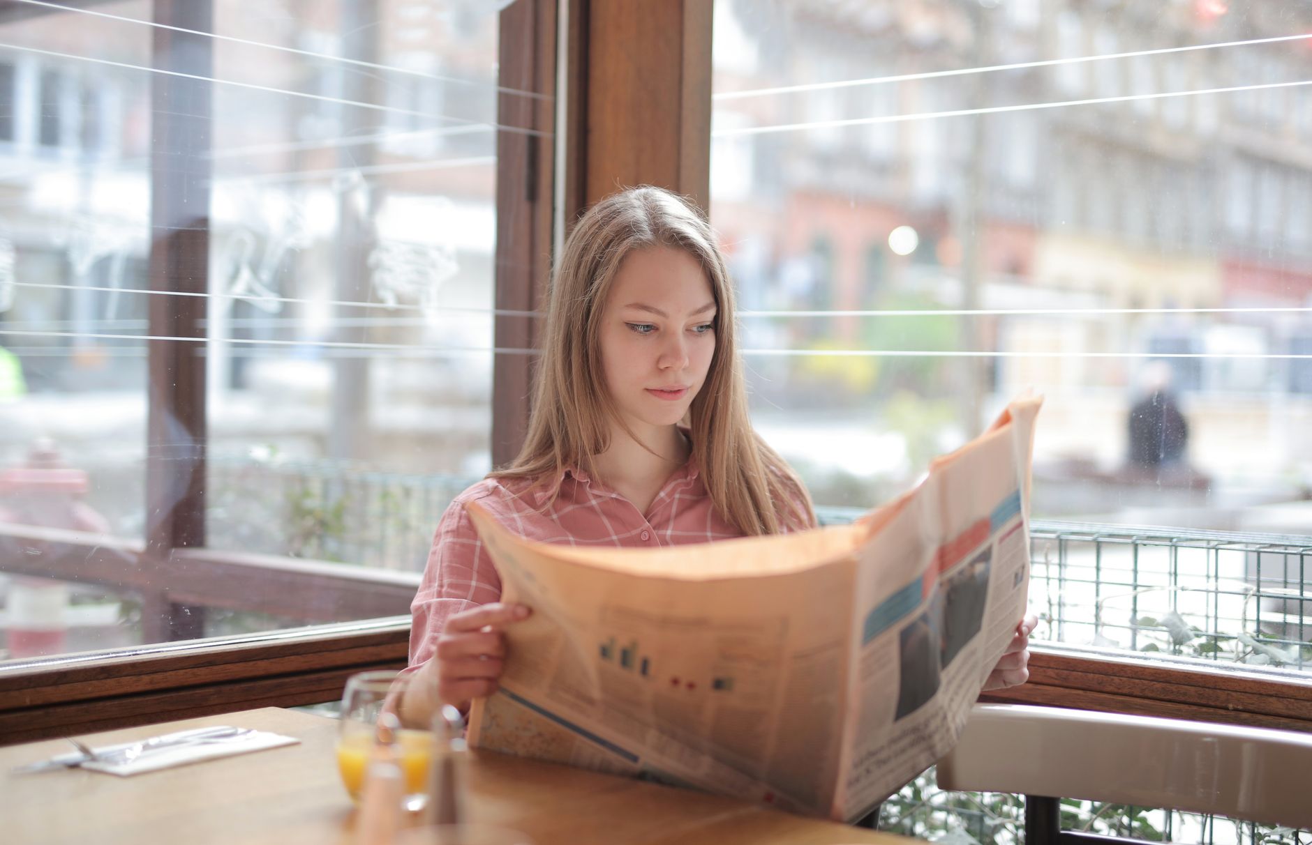 A young woman enjoying a newspaper at a cafe table, immersed in reading. — Replica Watches: An Affordable Luxury or a Costly