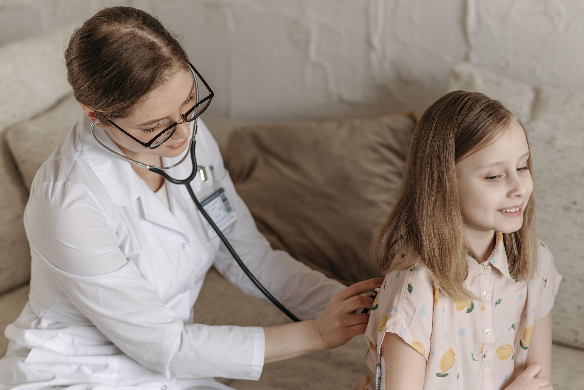 A doctor with a stethoscope examining a smiling girl during a medical check-up at home. — 5 Advantages of Laser Hair