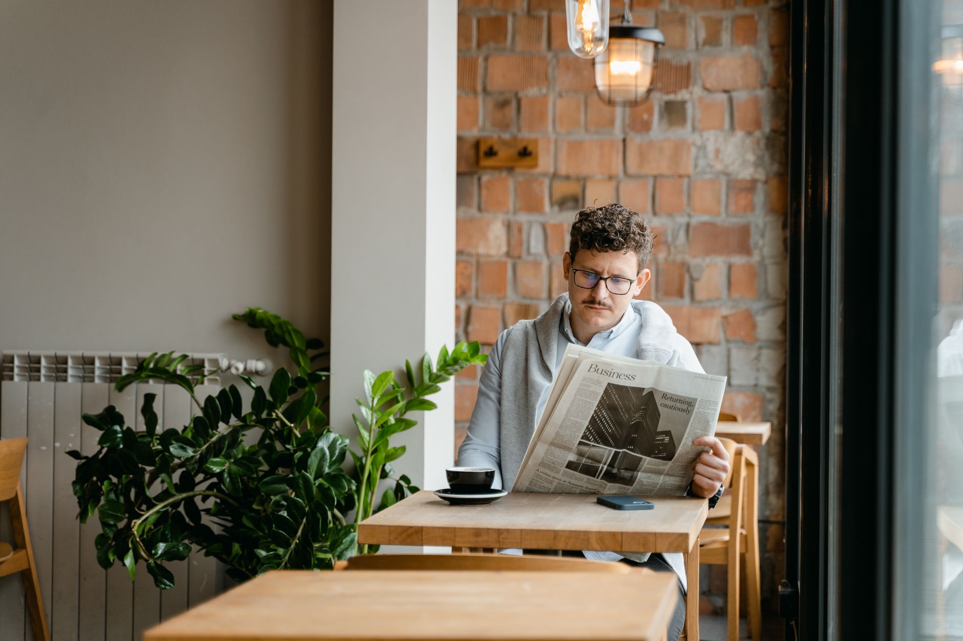 A man with glasses enjoys coffee and reads a newspaper in a cozy café setting. — Copycat Couture: Duplicated Louis Vu