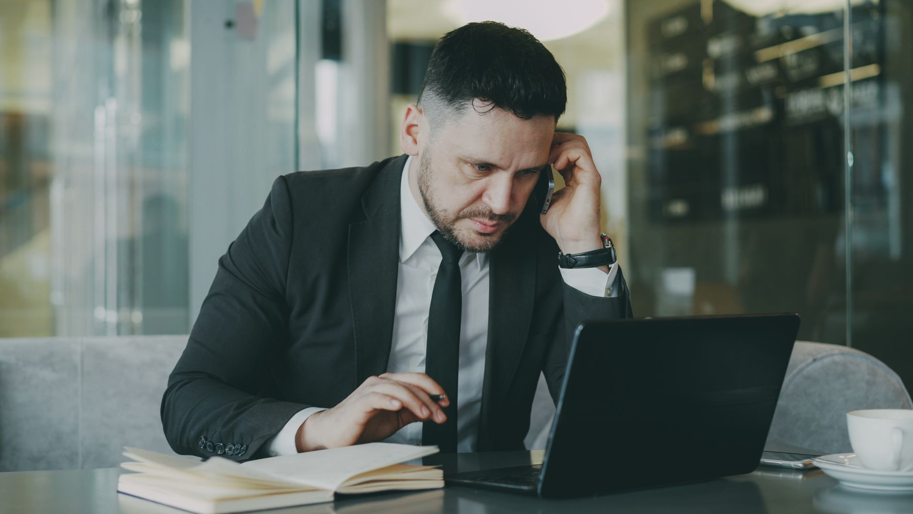 Focused businessman in suit multitasking on phone and laptop in modern office. — Find The Best 1 Person Shop Massage