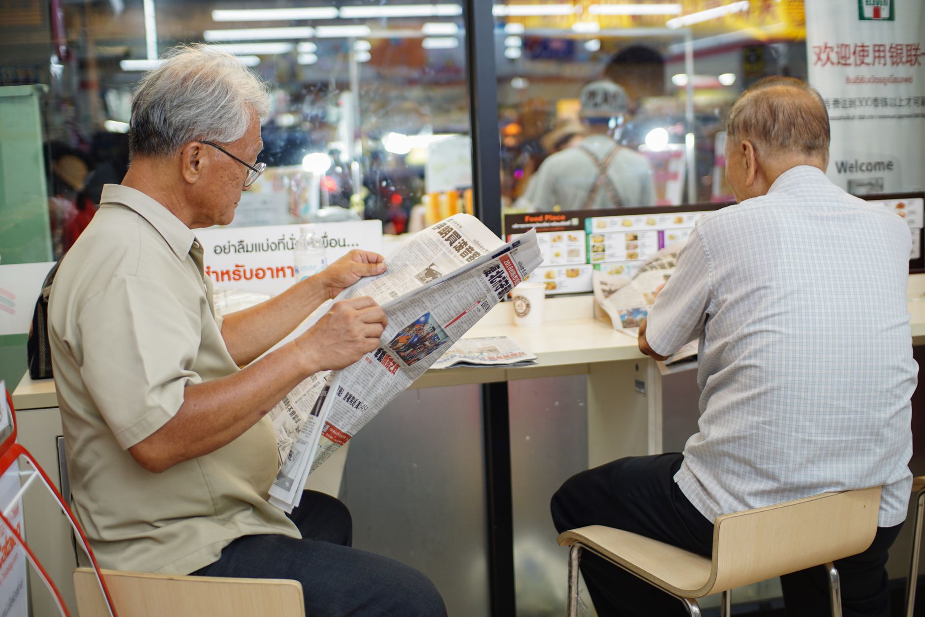 Two elderly men read newspapers inside a cafe in Bangkok, capturing a moment of daily life. — Superior Bathroom Faucet Instal