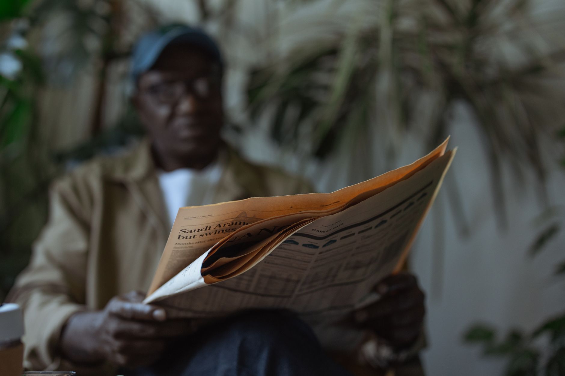 An adult man reading a newspaper indoors, surrounded by plants with a blurred background. — Swap and Exchange Crypto with Eas