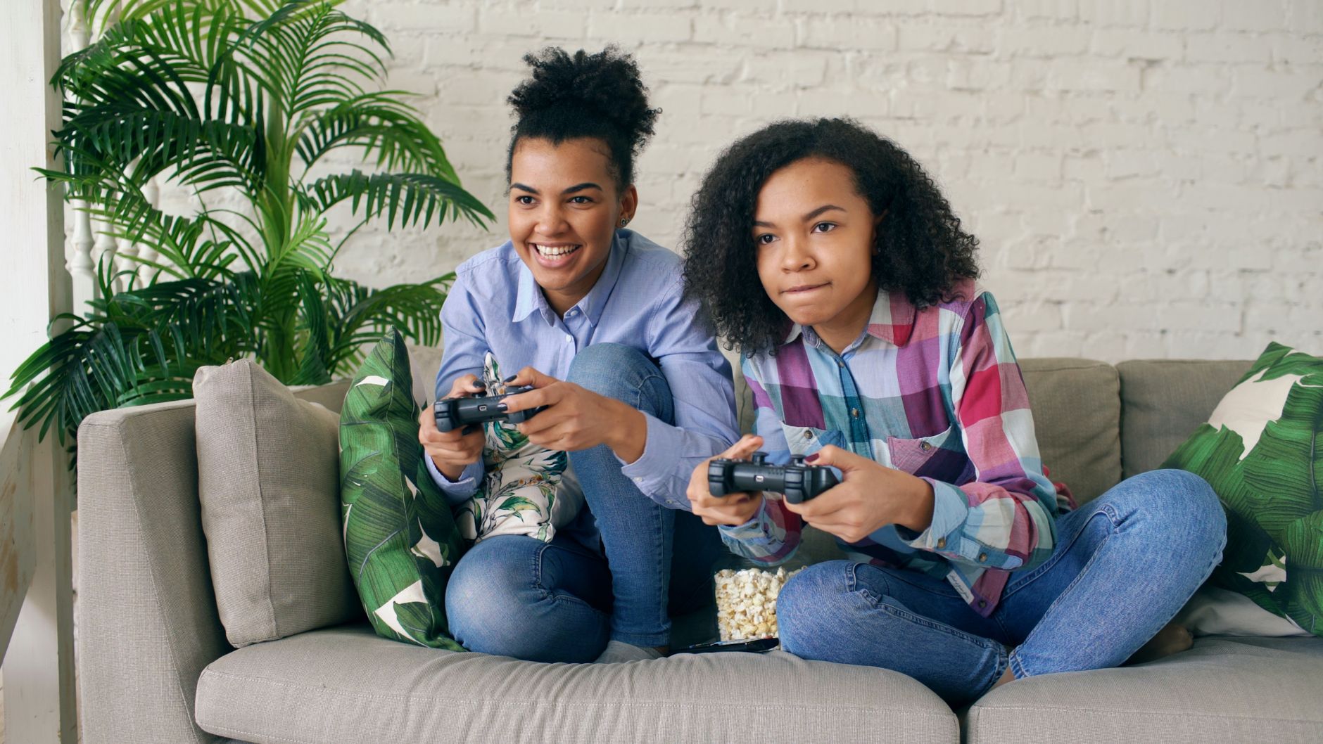 Two teenagers playing video games together on a comfortable couch, surrounded by indoor plants. — The Advantages of Playing a