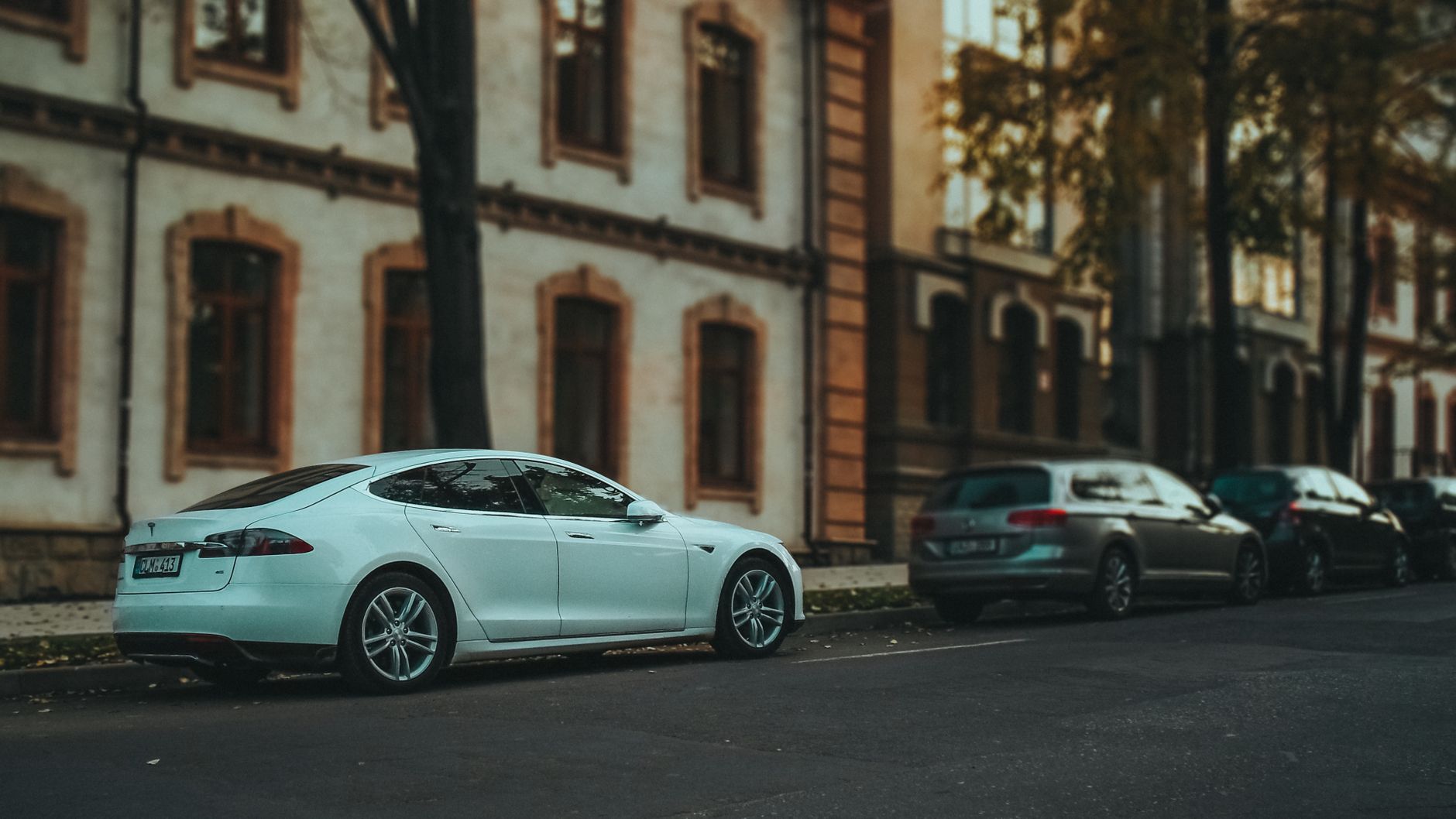 Side view of a sleek white sedan parked on a quiet urban street lined with trees. — Towing and Roadside Towing: Their Types
