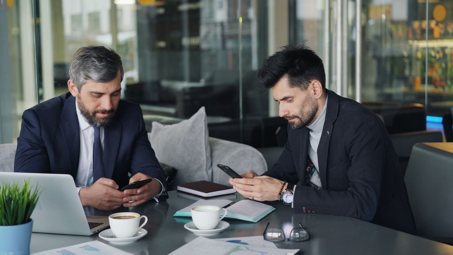 Two businessmen in a cafe working on smartphones and laptops, engaged in a meeting. — "Understand How to Navigate the Forex M