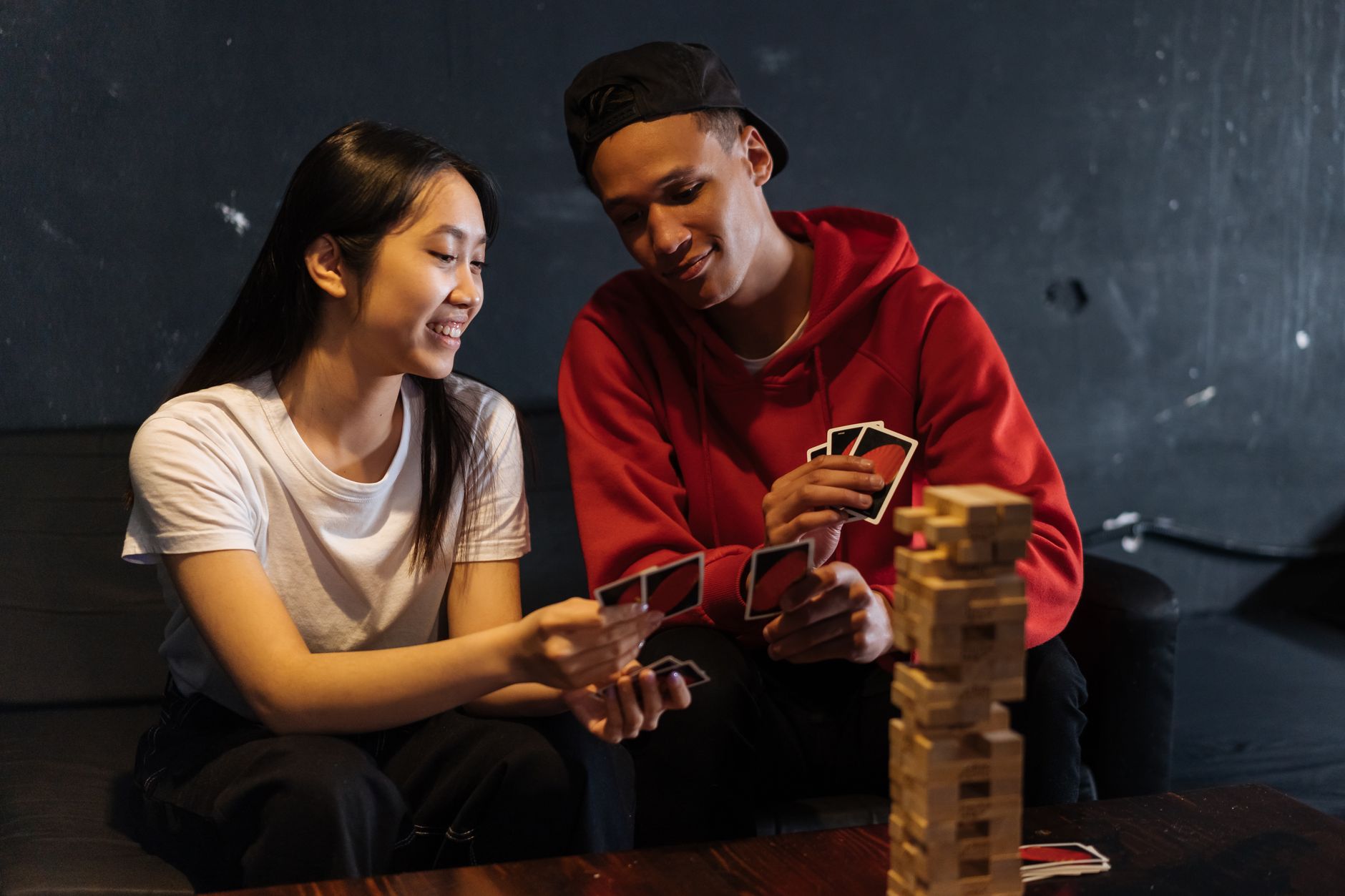 Two friends playing cards and Jenga indoors, sharing laughter and bonding over games. — What are the best football betting ti