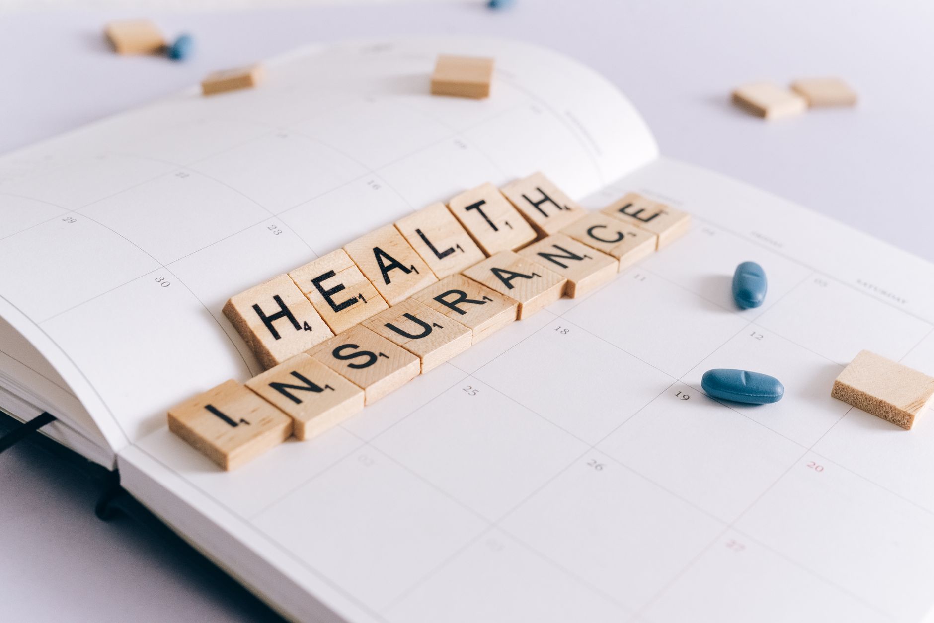 Scrabble tiles spelling 'Health Insurance' on a calendar with pills. — What Makes Bordeaux Wine So Great?