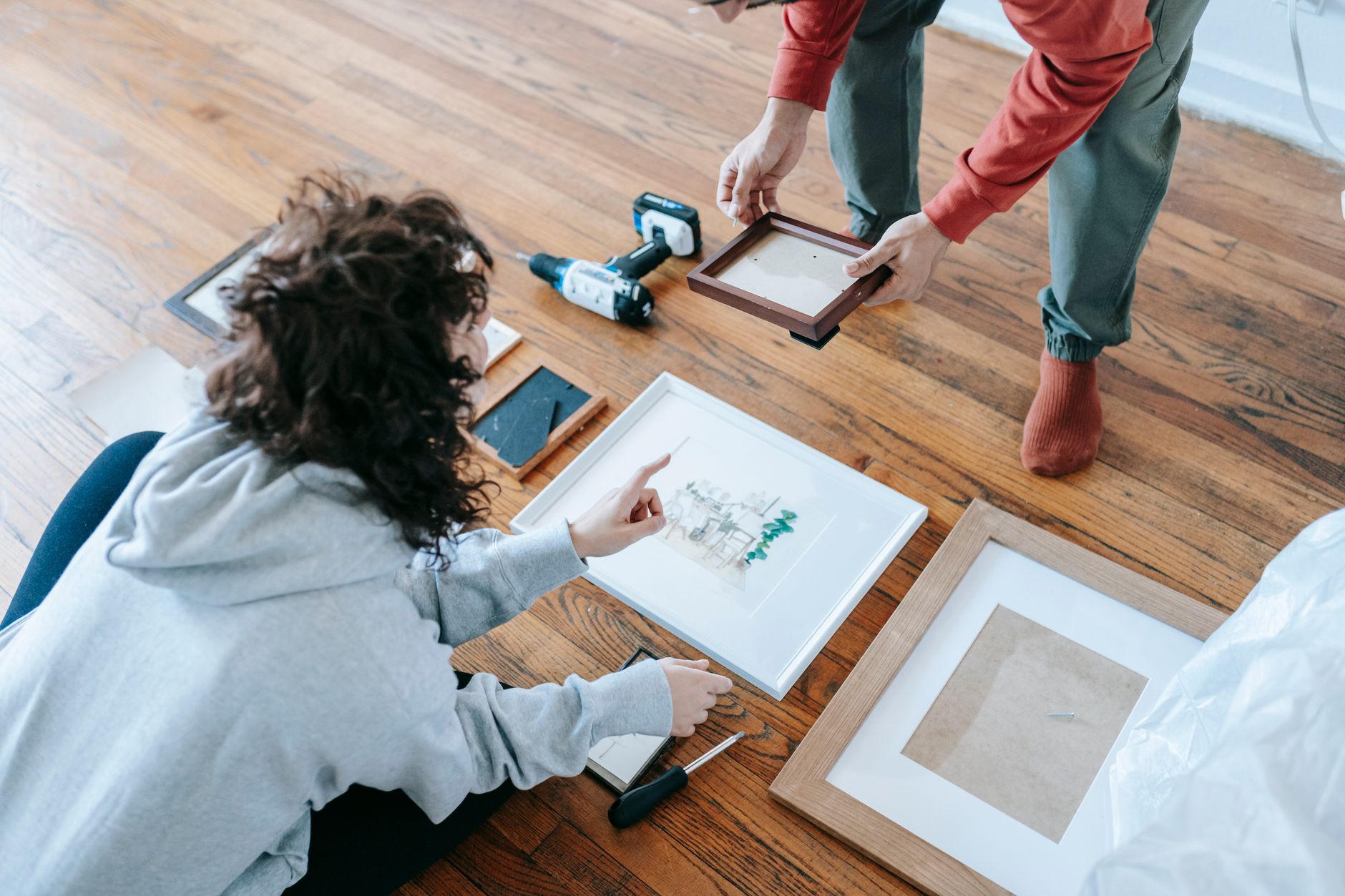 A couple organizing picture frames on a wooden floor, preparing for interior decoration or renovation. — When You Need A Plum