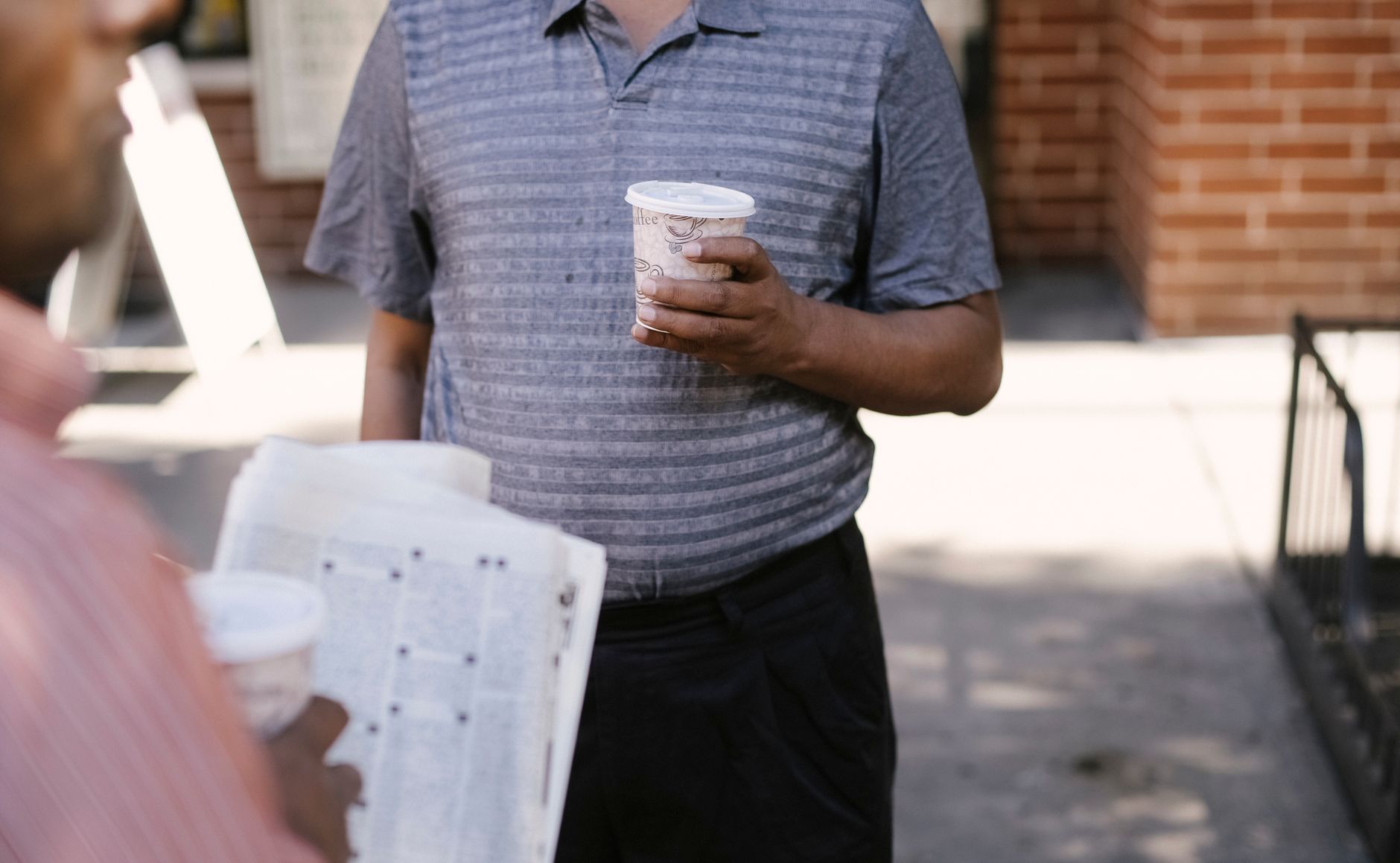 Crop anonymous ethnic male friends with coffee to go and newspaper speaking on city pavement — Why You Need To Use Paving Con